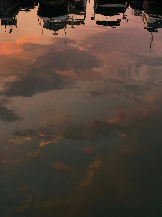 an orange sky reflecting off the water with several boats in it