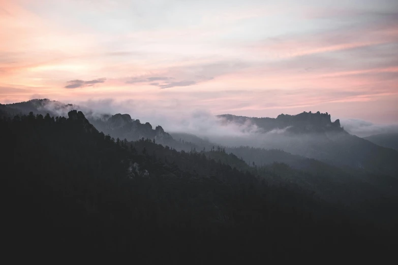 a pink sky with fog over trees and mountain range