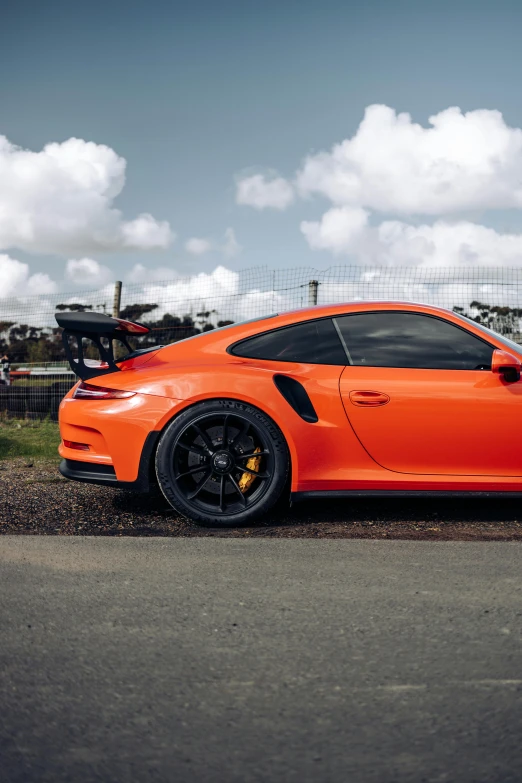 an orange porsche is parked in front of a large fence