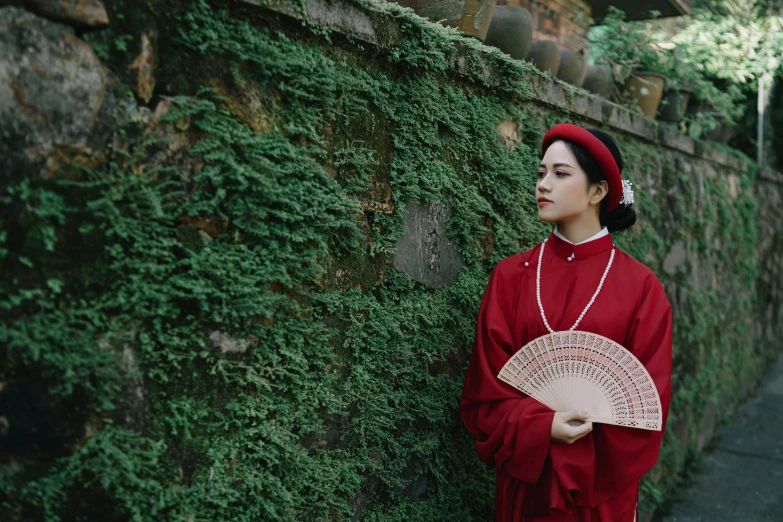 woman with red dress standing near a rock wall