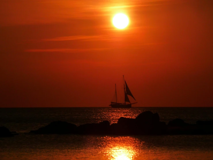 a small sail boat with its sails out and sun in the sky