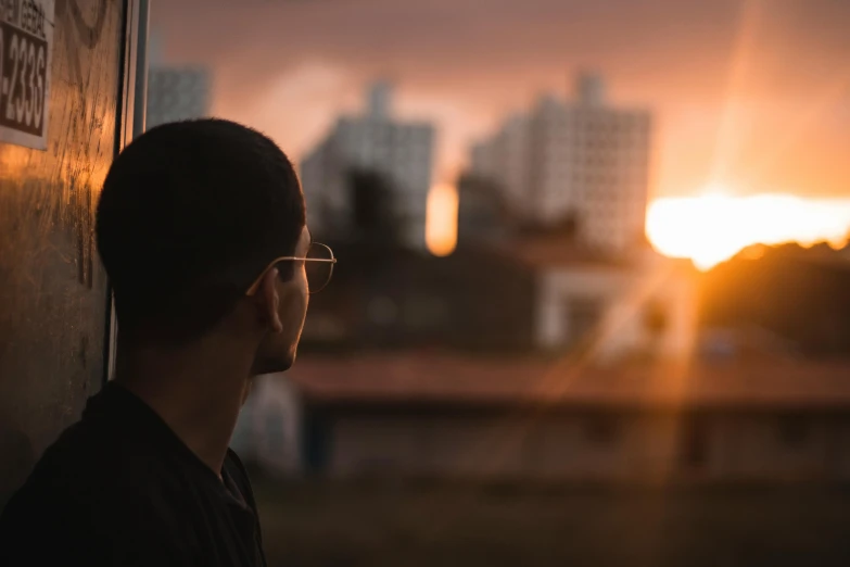 a man in glasses looking out over the city at sunset