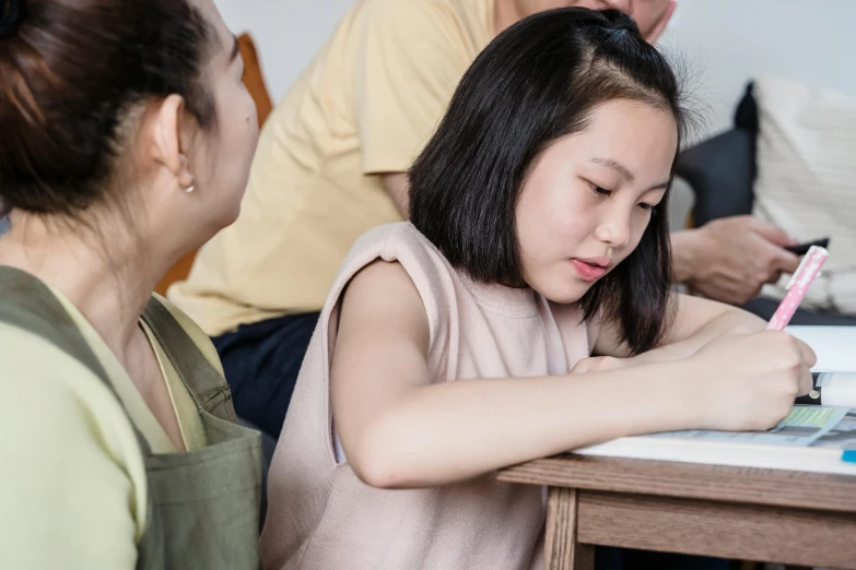 a girl sitting at a table writing and other children sit around