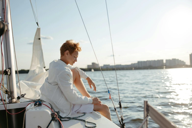 young man sitting on sailboat, on calm ocean