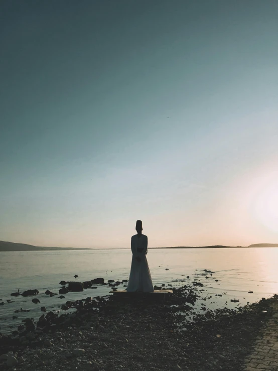 the silhouette of a woman standing near the water