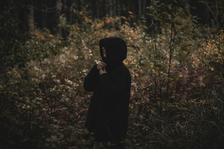 a person standing in a forest and holding a cigarette