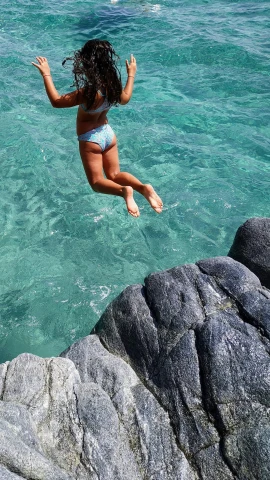 a girl in a swimsuit jumps into the ocean from a rocky cliff