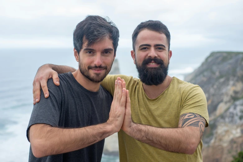 two guys standing together, one has his arms stretched out and the other is holding his hand up with both hands