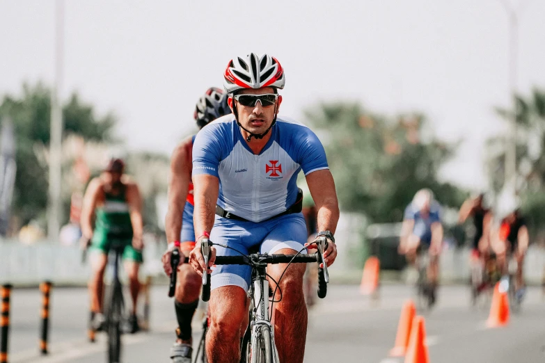 two men in helmets riding bicycles around orange cones