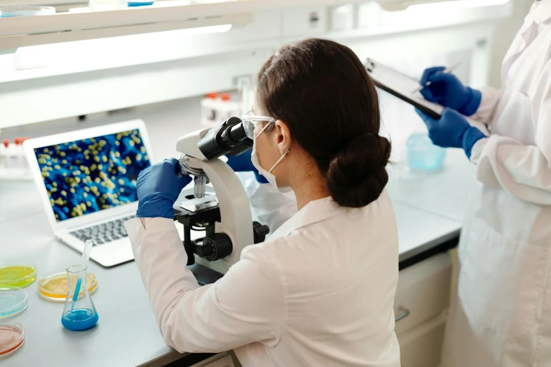 a laboratory worker working with a microscope in front of a laptop