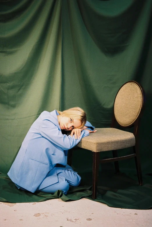 a woman with her head in her hands, sitting on a chair with a cloth covered backdrop