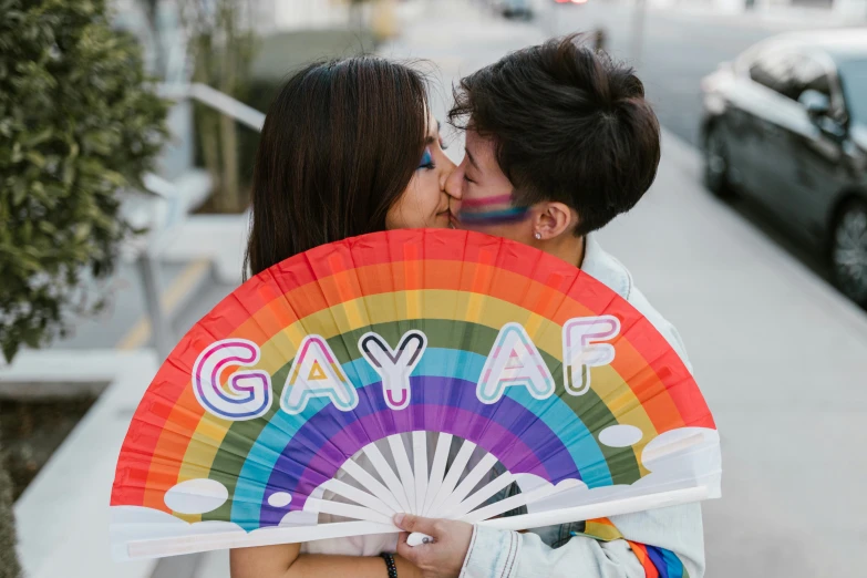 two people kissing and holding an rainbow fan