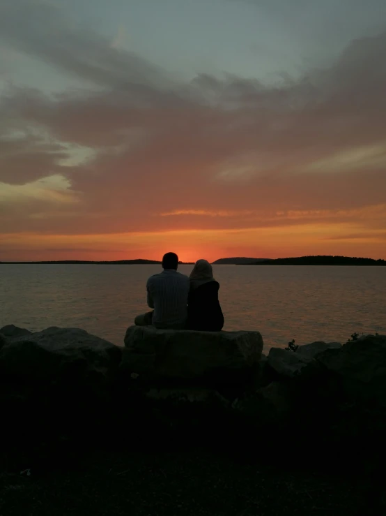 two people sitting on rocks watching a sunset at the beach