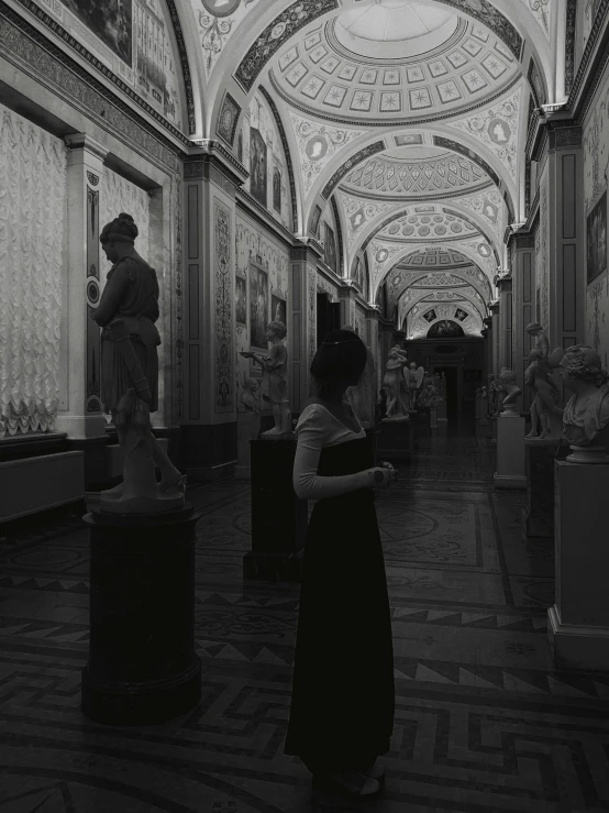 black and white po of woman standing in front of statues in museum