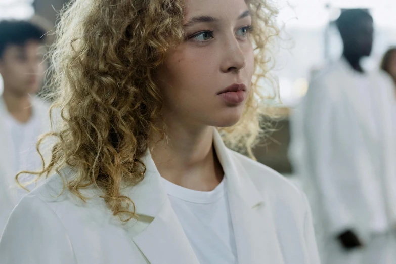 woman with curly hair and white suit standing in front of other people