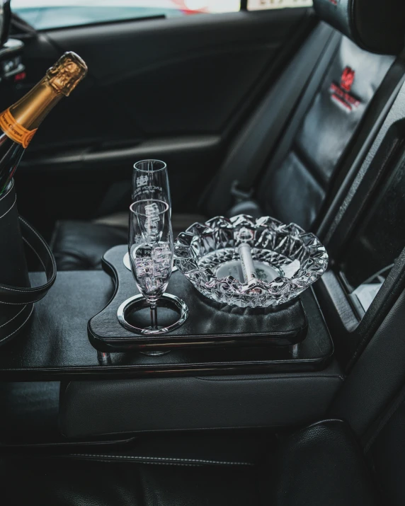 two champagne glasses and two crystal dishes sit on a black table in the backseat of a car