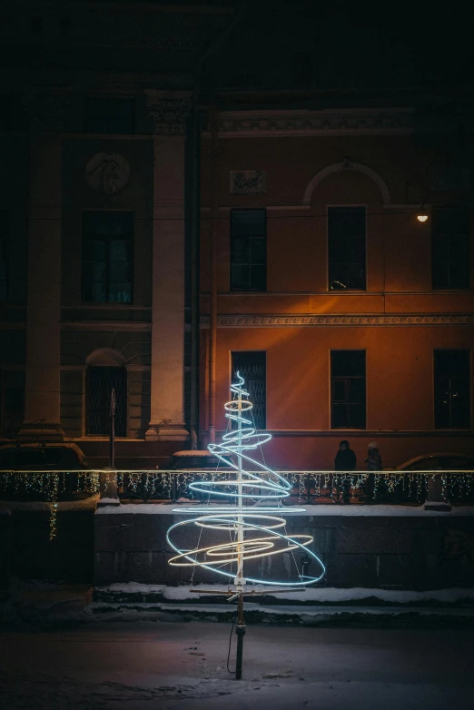 a lit christmas tree sits on the pavement in front of an apartment building