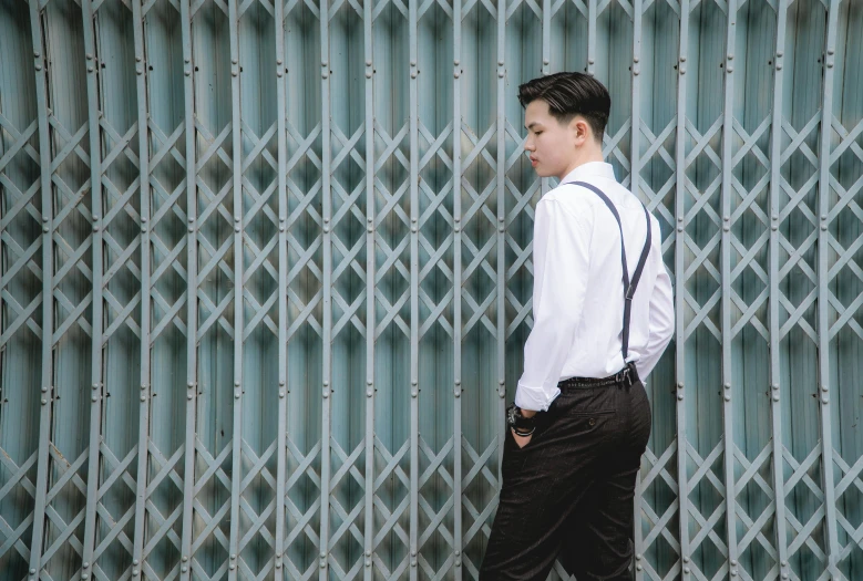 man in formal wear with suspenders and a bow tie against a building wall