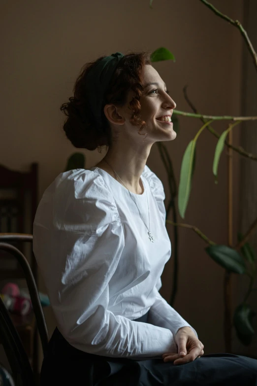 a woman is looking to her left with greenery behind her