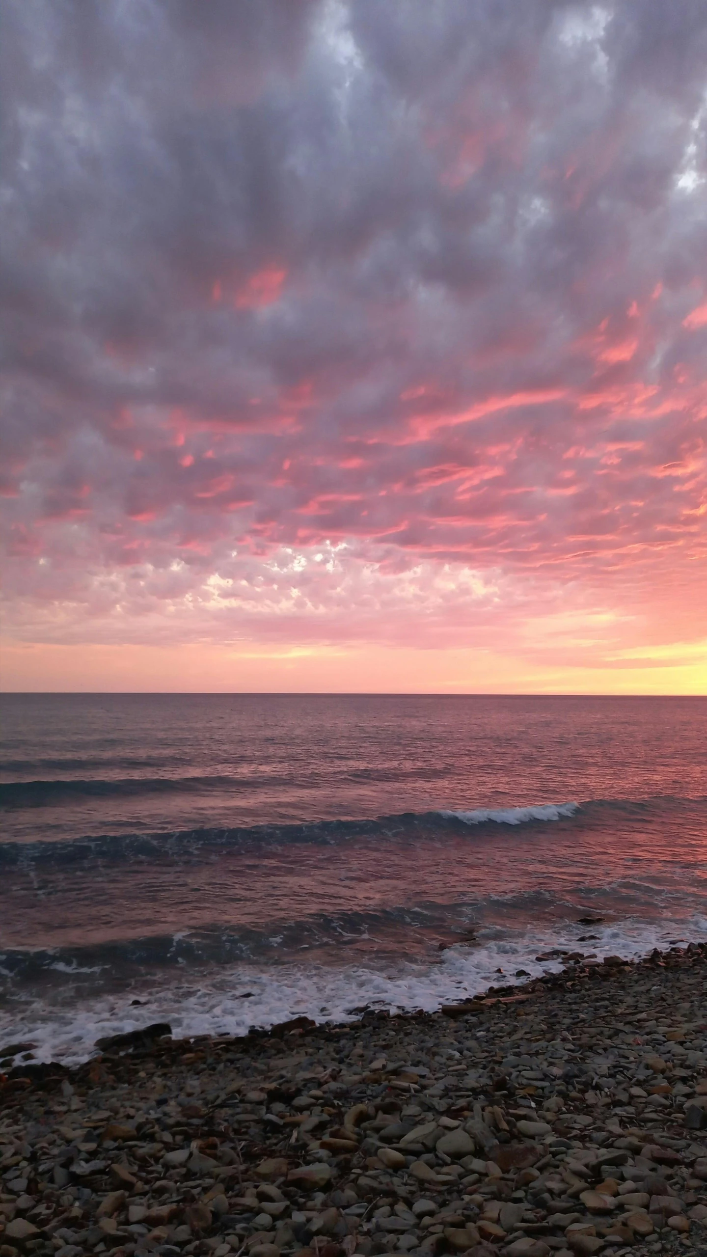 a beach with a very large body of water and some red clouds