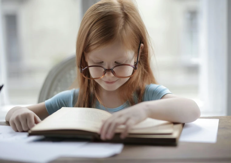 the little girl is sitting at the table with her book