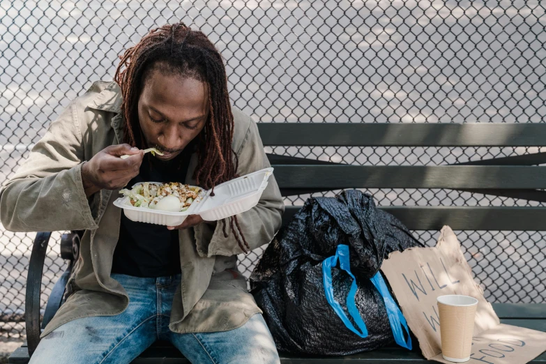 the woman in the jacket is eating cereal on a park bench