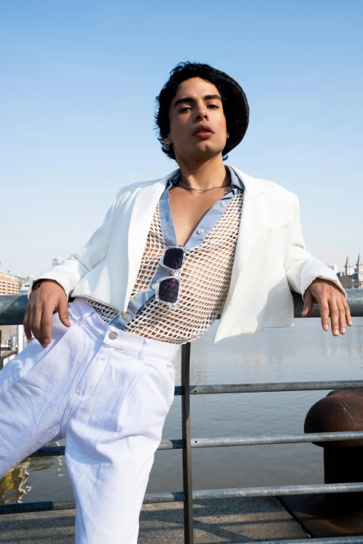 a man leaning on a fence wearing a white suit and black hat