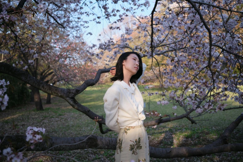 an asian woman in white clothing standing under a blossoming tree