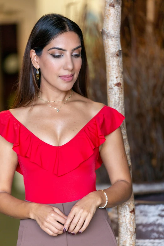 a woman with an elegant red top and earrings holding hands near a tree