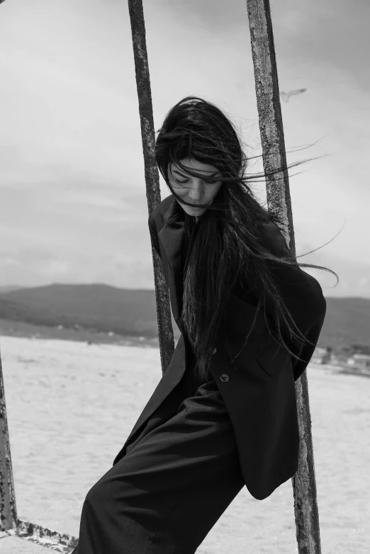 a woman is leaning against a pole by the water