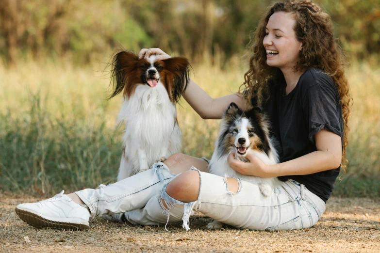 a woman in ripped denims holds her two dogs while sitting on the ground