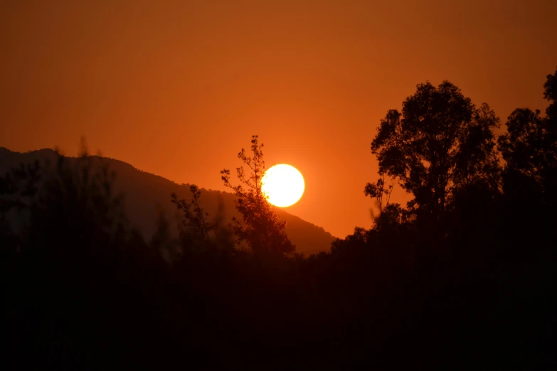 the sun is rising behind some trees and hills