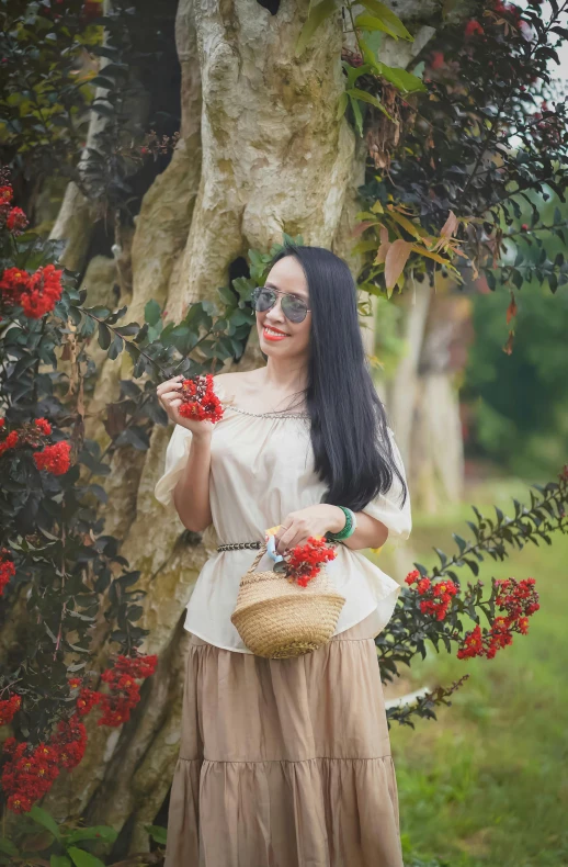 a young woman dressed up in a white top holds a flower bouquet near a tree