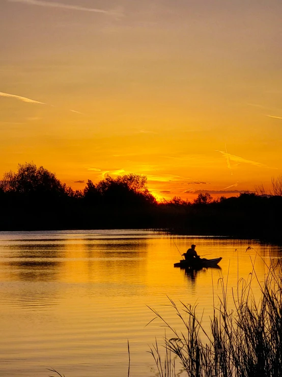 a man in a boat on a calm lake at sunset