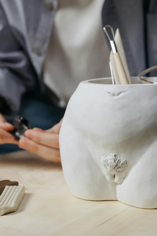 a person in a grey jacket working on a white sculpture