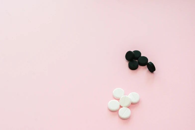 some pills on pink background and one is green and the other has white