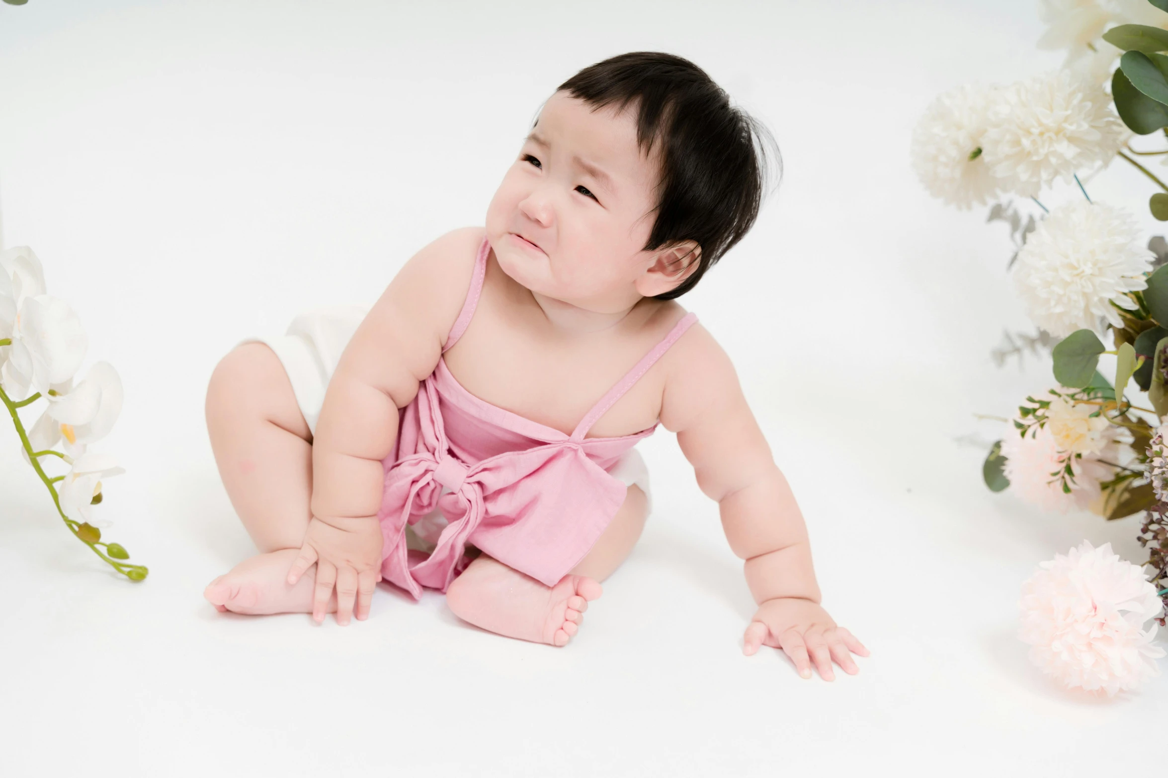 a small child with pink clothes sits in front of some flowers