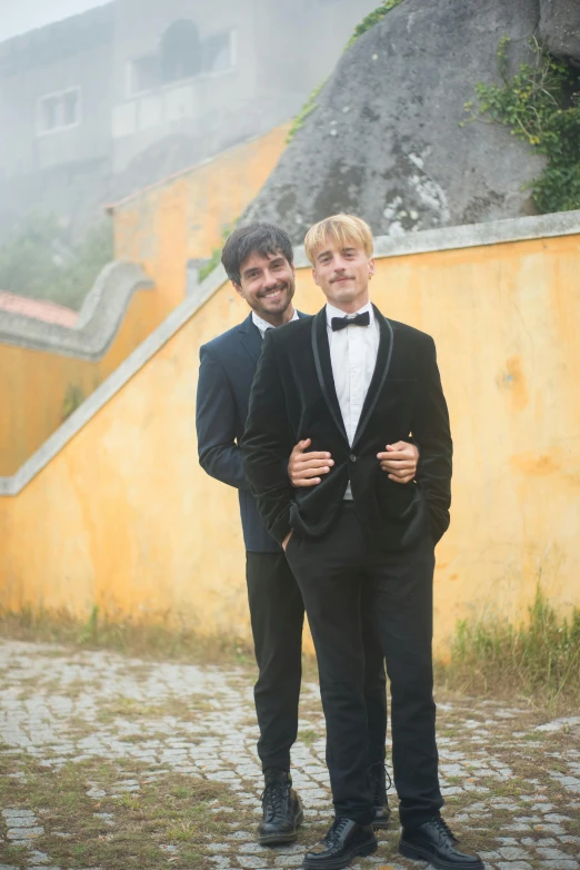 two men wearing tuxedos are standing in front of a yellow wall