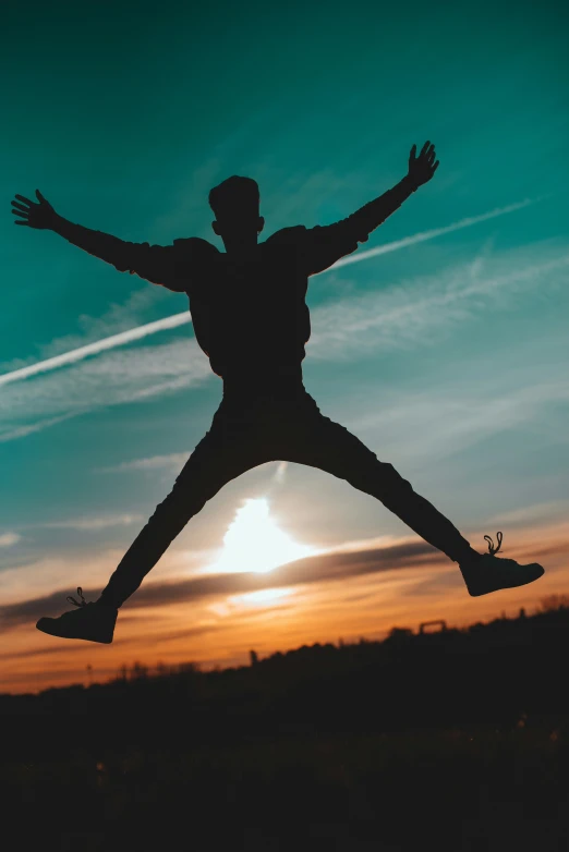 a silhouette of a person jumping and holding his arms out in front of the sun