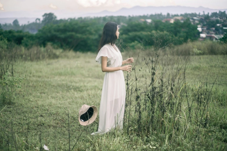 woman in dress holding hat walking through a field