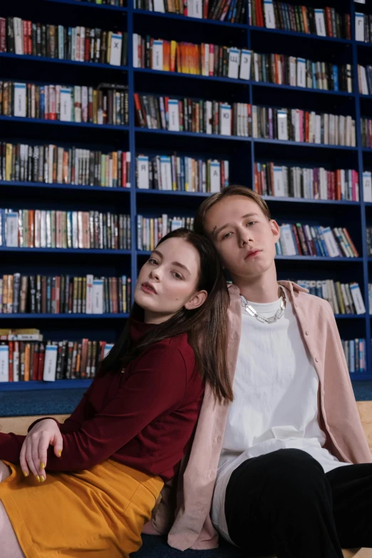 a couple is sitting on the floor in front of a book shelf