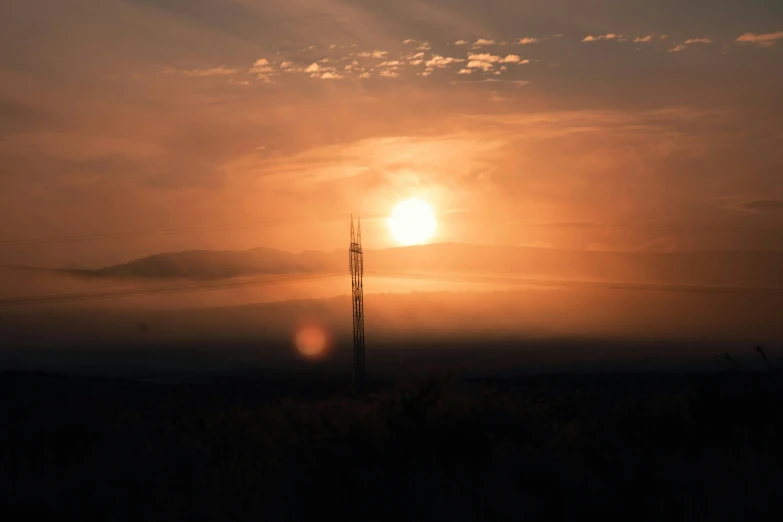 the sun rising behind an area with a power pole