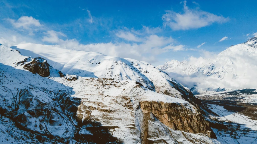 a scenic mountain range covered in snow under a partly cloudy blue sky