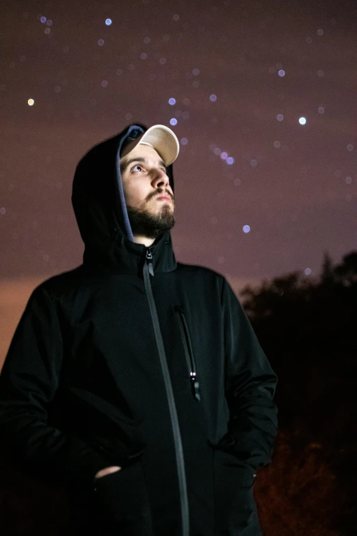 man in hoodie posing in front of sky filled with stars