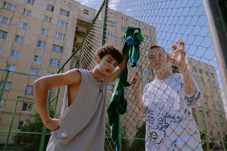 two boys are posing against a fence with some buildings in the background