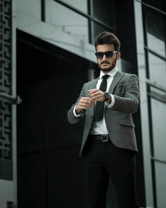 man in a gray suit and black sunglasses adjusting his tie