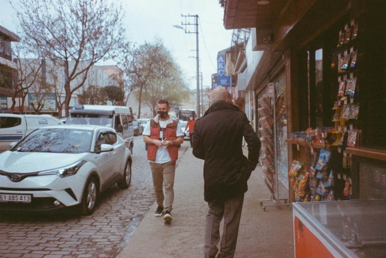 two men walking down the sidewalk by a car