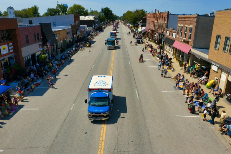 a blue truck driving down a road surrounded by people