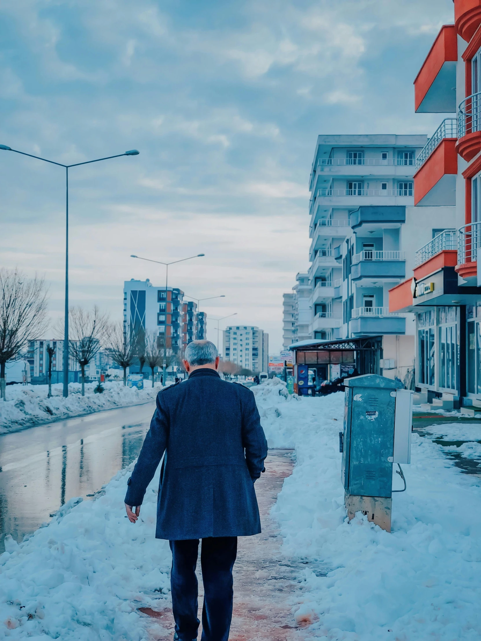 man walking in the snow on a walkway between a sidewalk and buildings