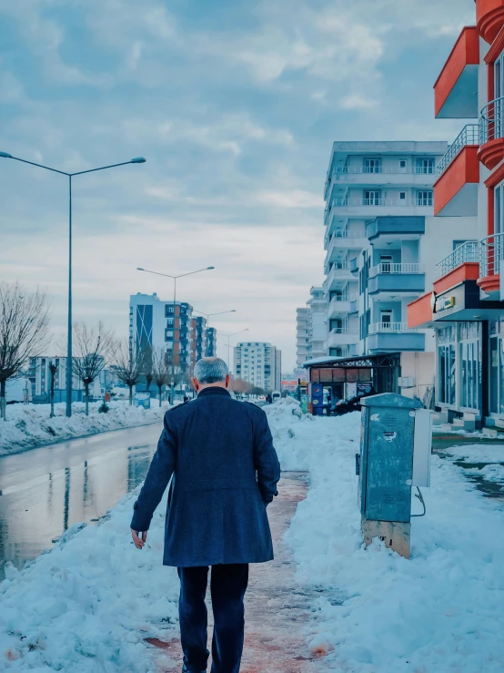 man walking in the snow on a walkway between a sidewalk and buildings